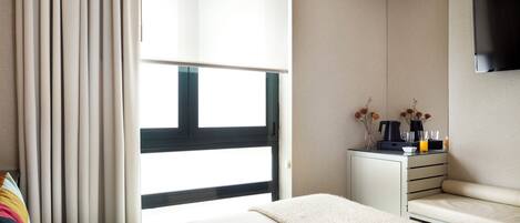 A modern hotel room with a bed, a sofa, a small desk with a coffee maker, and a TV mounted on the wall.