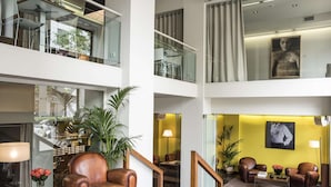 A spacious lobby with a high ceiling, a staircase, leather armchairs, a coffee table, and a large painting on the wall. - Hotel Miro (Bilbao)