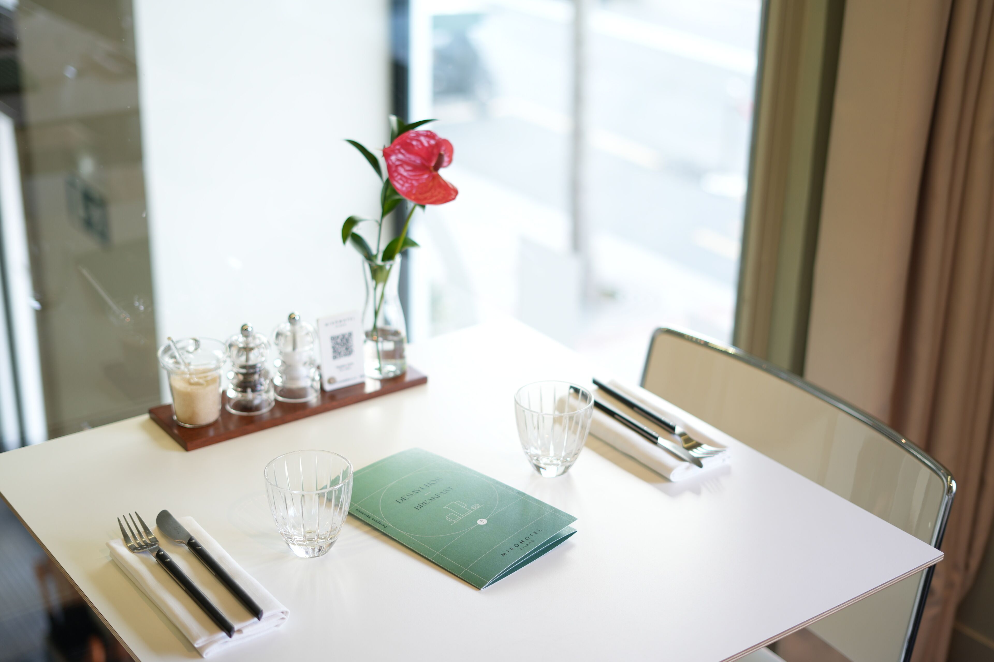 A neatly set dining table with a menu, cutlery, and a vase with a single flower.