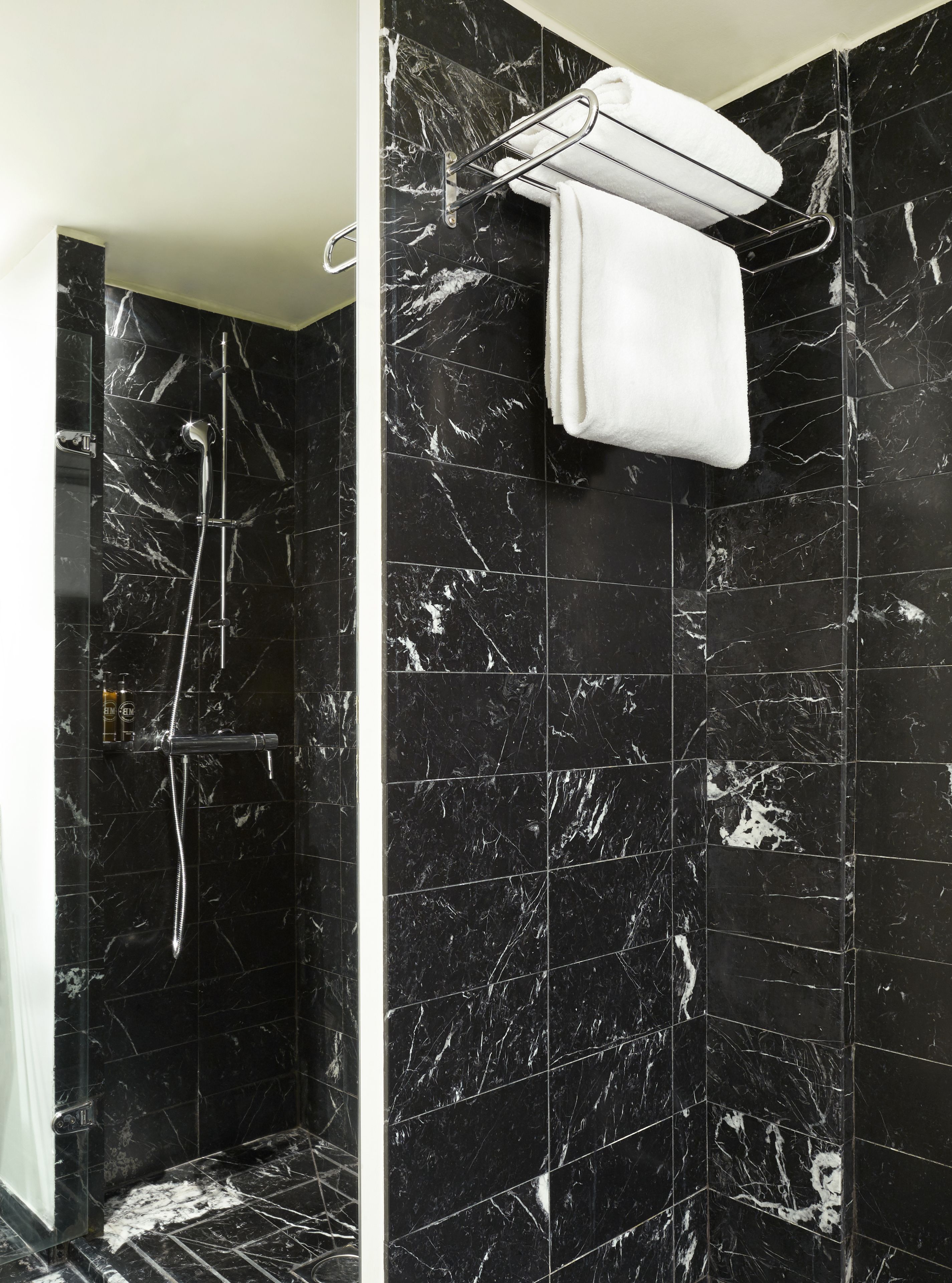 Un bagno moderno con piastrelle in marmo nero, cabina doccia in vetro e porta asciugamani con un asciugamano bianco.