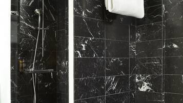 Un bagno moderno con piastrelle in marmo nero, cabina doccia in vetro e porta asciugamani con un asciugamano bianco.
