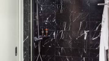 Une salle de bain moderne avec des carreaux de marbre noir, une douche en verre et une serviette blanche suspendue à un porte-serviettes.