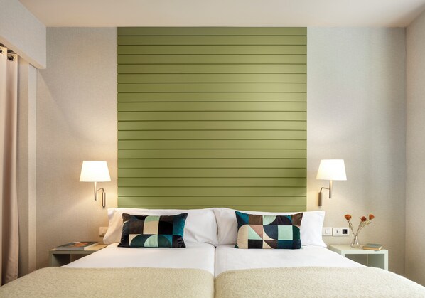A double bed with two pillows, a nightstand with a lamp, and a small table with a vase of flowers.