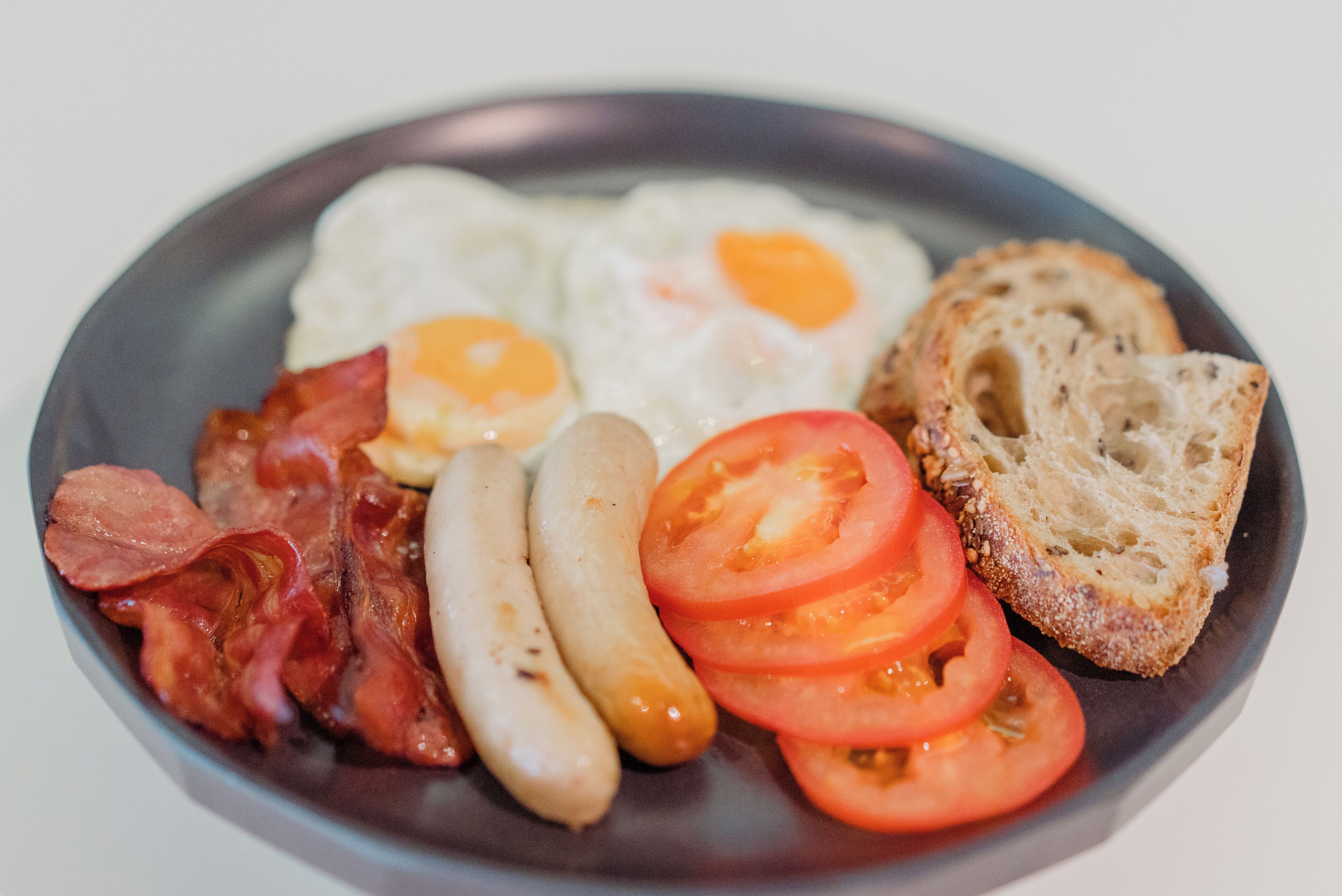 A plate with eggs, bacon, sausages, tomatoes, and toast.