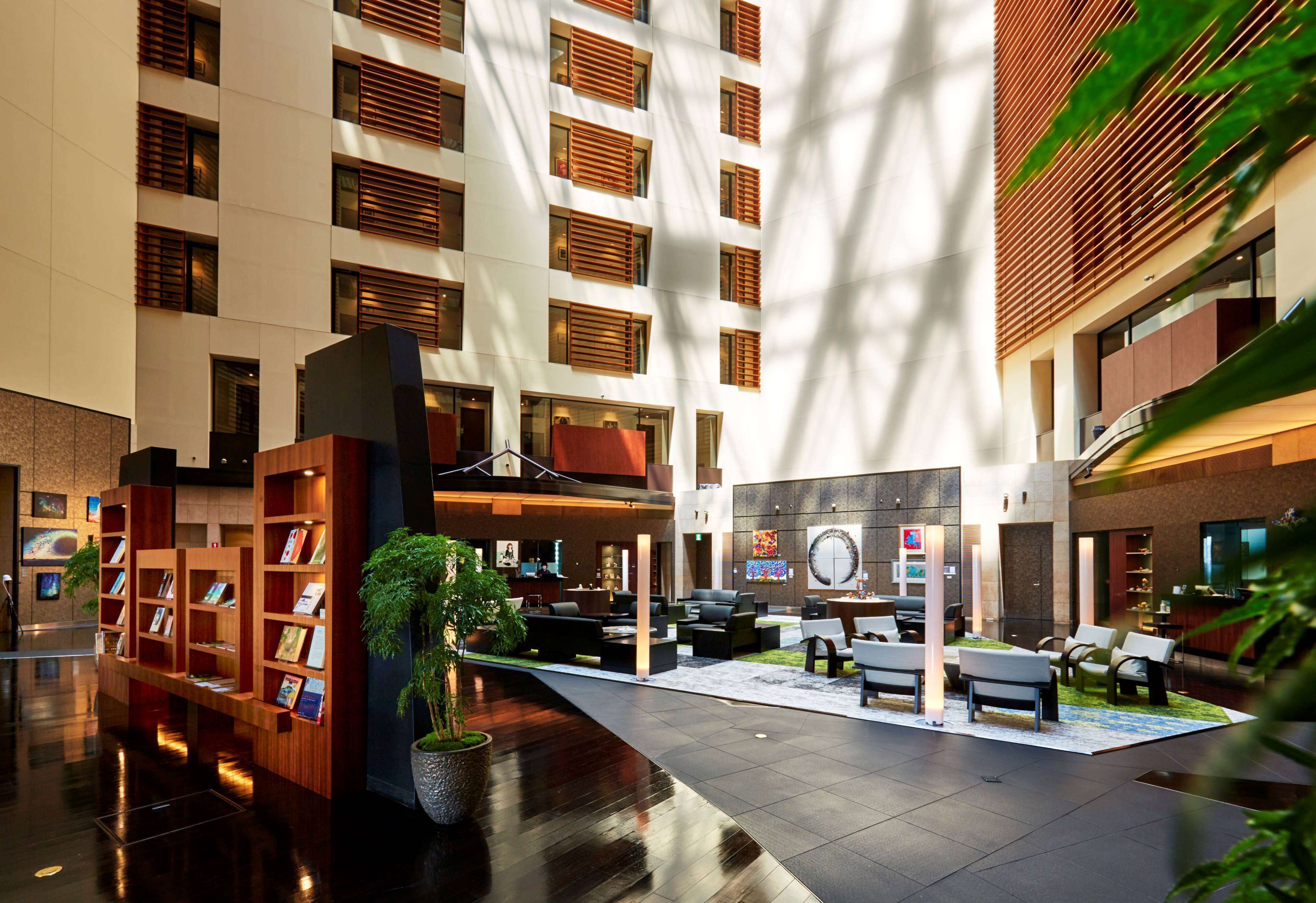 A modern hotel lobby with a central seating area, a reception desk, and a bookshelf.