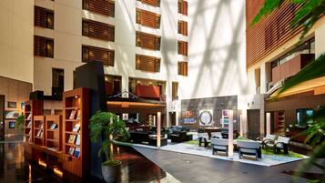 A modern hotel lobby with a central seating area, a reception desk, and a bookshelf.