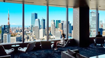 A modern hotel room with large windows offering a cityscape view, including a prominent tower.