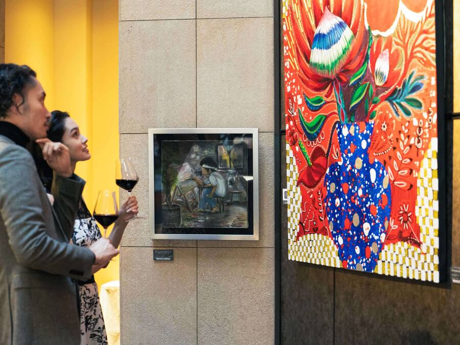 A framed artwork depicting a scene with a person painting, placed on a wall with a colorful mural to the right.