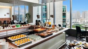 A modern hotel breakfast buffet with a city view, featuring a variety of food items and a seating area. - Park Hotel Tokyo (Tokyo)
