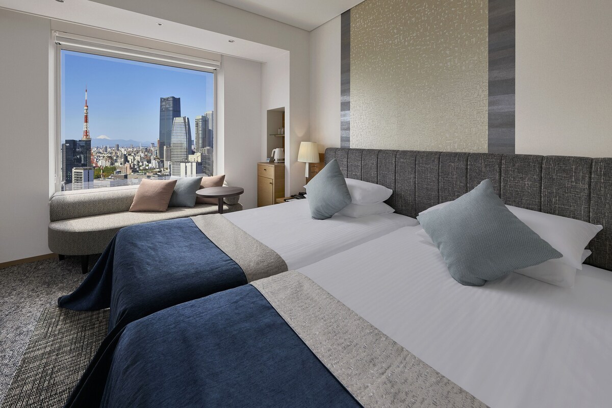 A hotel room with a city view, two beds, a sofa, and a small table.