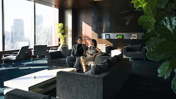 A modern lounge area with a city view, comfortable seating, and a large plant.
