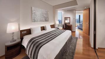 Ein modernes Hotelzimmer mit einem großen Bett, einem Schreibtisch, einem Stuhl, einer Lampe, Blick auf die Stadt und einer Tür zu einem weiteren Raum.