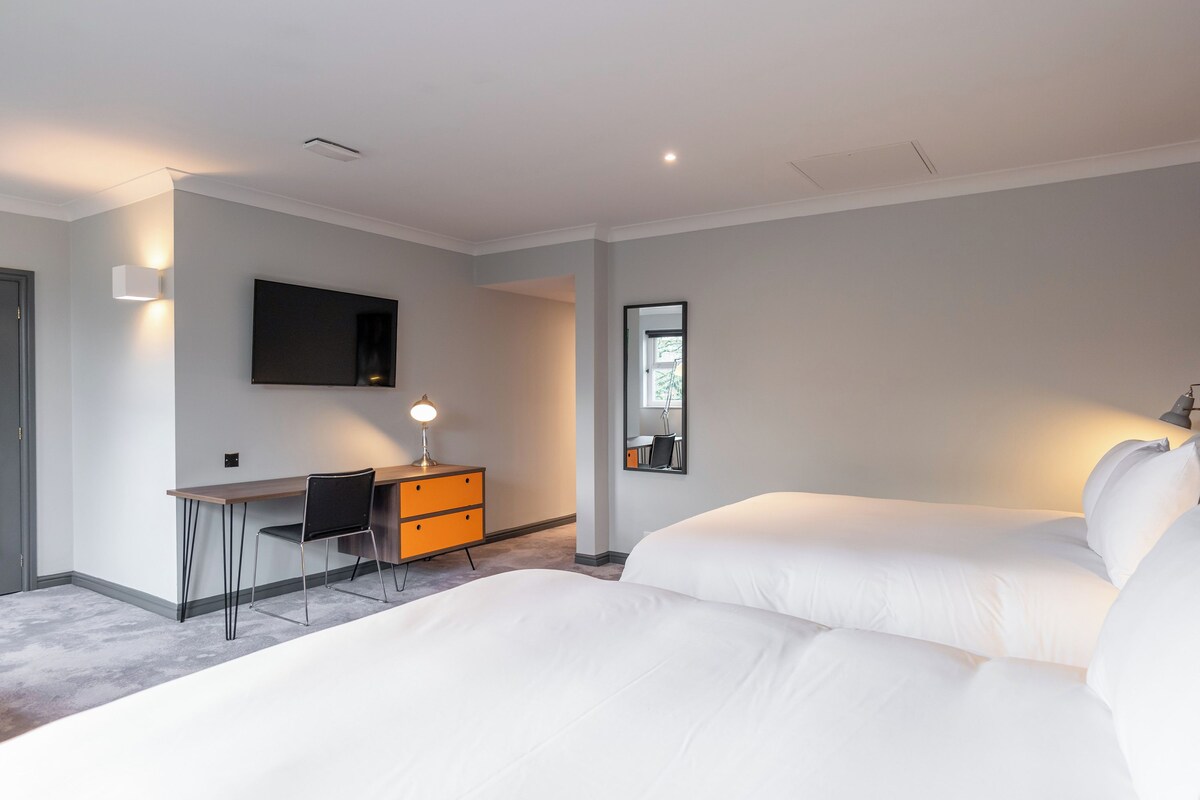 Une chambre d’hôtel moderne dotée d’un grand lit, d’un bureau avec une chaise, d’un téléviseur à écran plat et d’un miroir.
