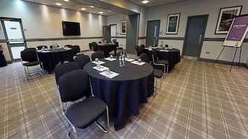 A conference room with round tables, chairs, and a presentation screen.