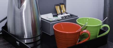 A black tray with a stainless steel coffee maker, a red mug, and a green mug.