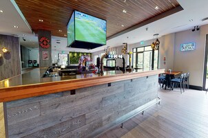 Un área de bar moderna con un mostrador de madera, una pantalla de televisión grande y un letrero de 'Bud Light'.