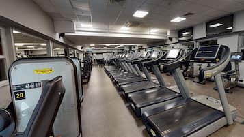 A gym with multiple treadmills lined up in rows, equipped with digital displays and weight machines.
