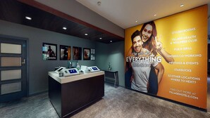 A hotel reception area with a large poster advertising various amenities such as stylish rooms, a village health and wellness club, a pub and grill, and a Starbucks. - Village Hotel St David's, Nr Chester (Deeside)
