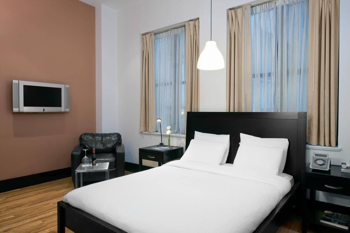 Una habitación de hotel moderna con una cama grande, un televisor de pantalla plana, un escritorio con lámpara y una silla.