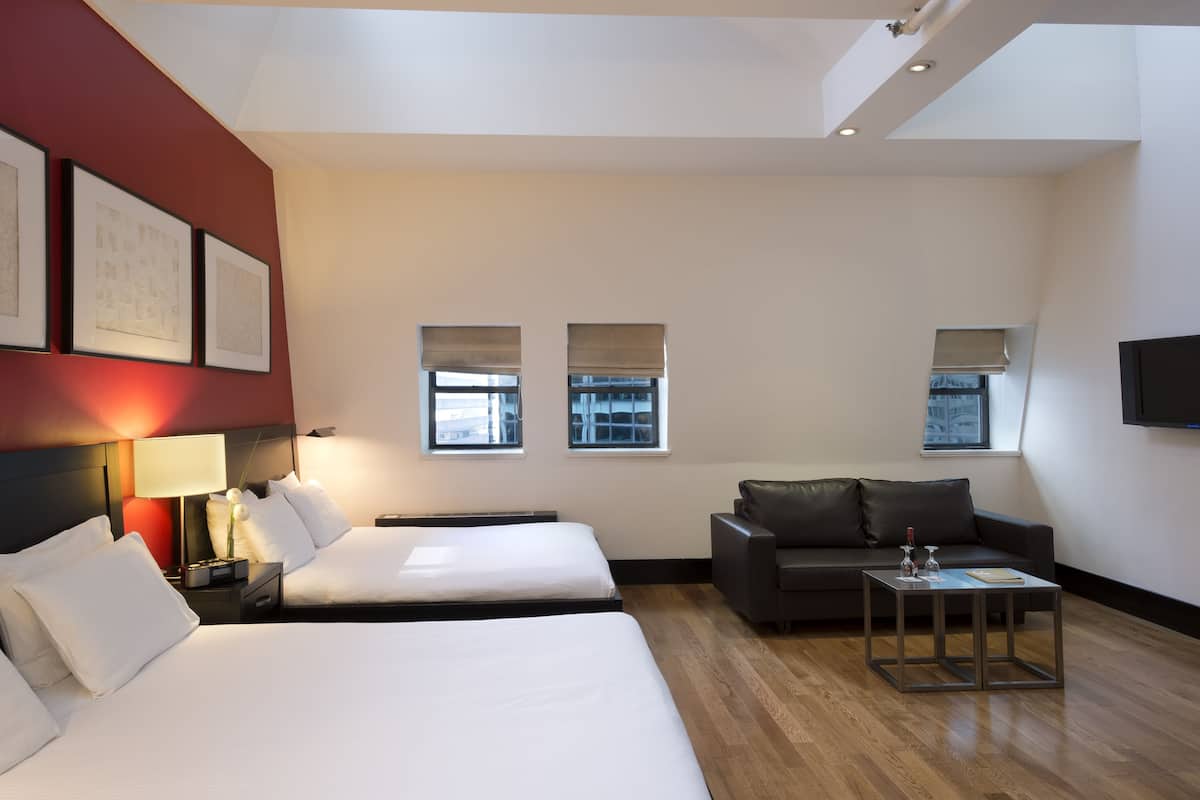 Una habitación de hotel con dos camas, un sofá, una mesa de centro y un televisor en la pared.