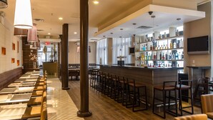 A modern bar area with a long counter, multiple stools, and a variety of bottles on shelves.