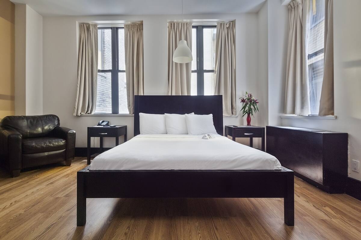 Un dormitorio moderno con una cama grande, un sillón de cuero y un escritorio con una lámpara.
