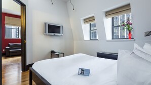 A hotel room with a large bed, a TV mounted on the wall, a window with a view of buildings, and a small table with a phone.