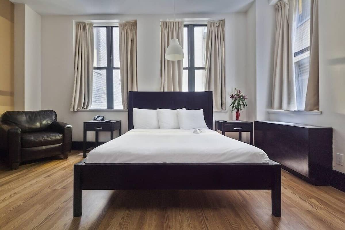 Una habitación de hotel moderna con una cama grande, un sillón de cuero, dos mesitas de noche y una planta en maceta.