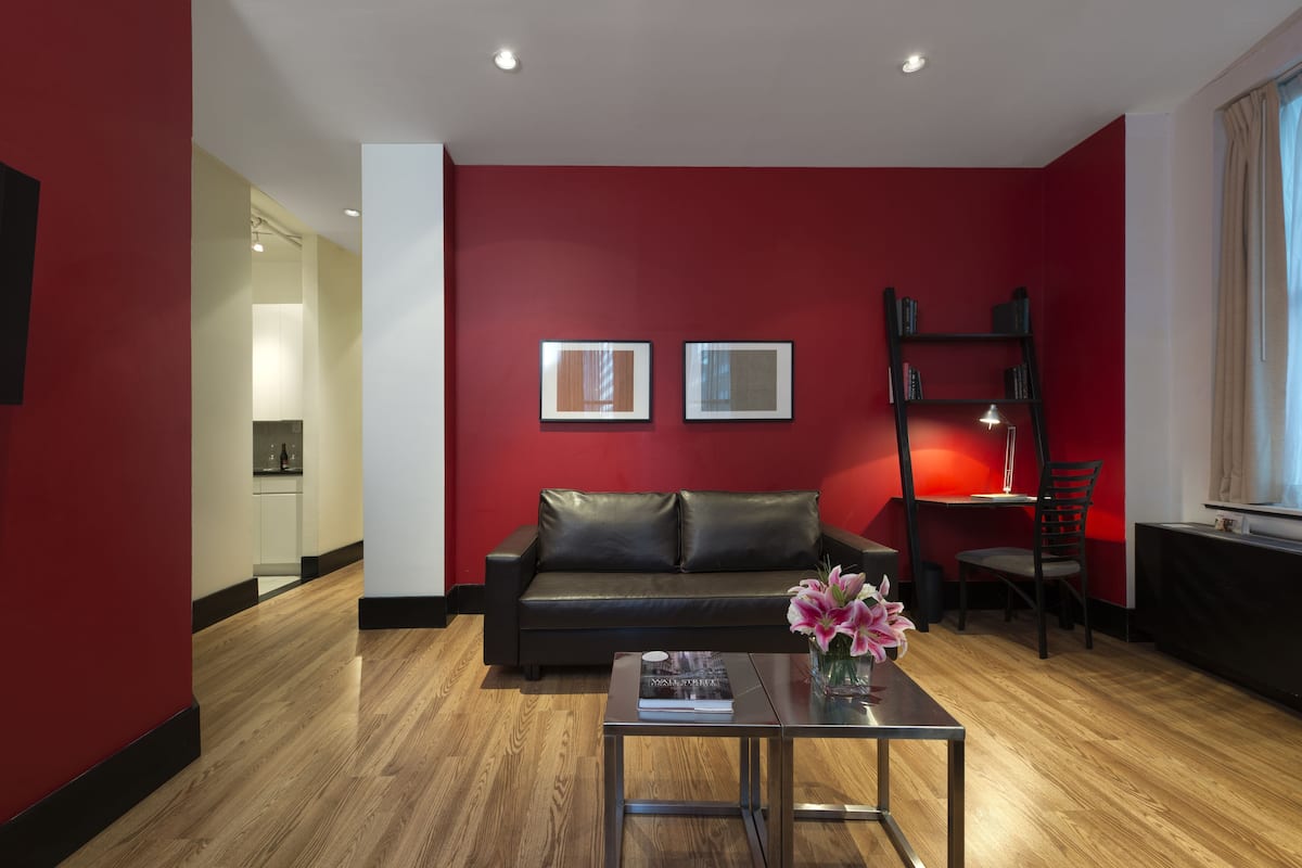 Una sala de estar moderna con una pared de acento roja, un sofá de cuero negro, una mesa de centro de vidrio con un libro y flores, y una estantería.