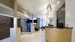 A modern hotel lobby with a reception desk, seating area, and a staircase.