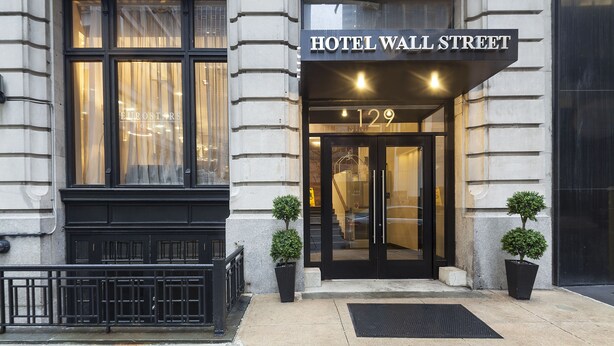 The entrance of Hotel Wall Street with a black facade, large windows, and two potted plants.