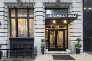 The entrance of Hotel Wall Street with a black facade, large windows, and two potted plants.