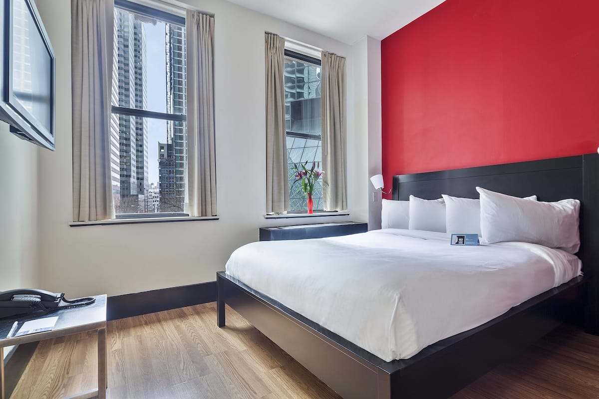 Una habitación de hotel moderna con una cama grande, un escritorio y dos ventanas con cortinas.