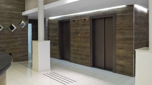 A modern elevator area with three elevators, a white pillar, and a wooden wall.