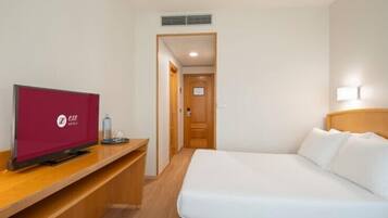 A hotel room with a bed, a desk with a television, and a door leading to another room.