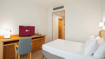 A hotel room with a bed, a desk with a computer, a chair, and a door.