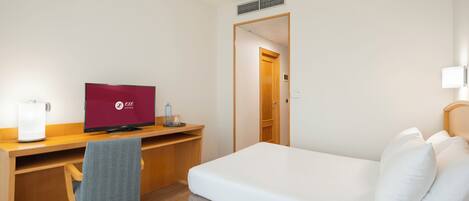Una habitación de hotel con cama, escritorio, computadora, silla y puerta.