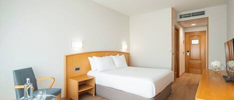 A hotel room with a bed, a chair, a small table, and a wooden desk.
