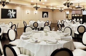 Un salón de banquetes con mesas redondas, manteles blancos y sillas negras.