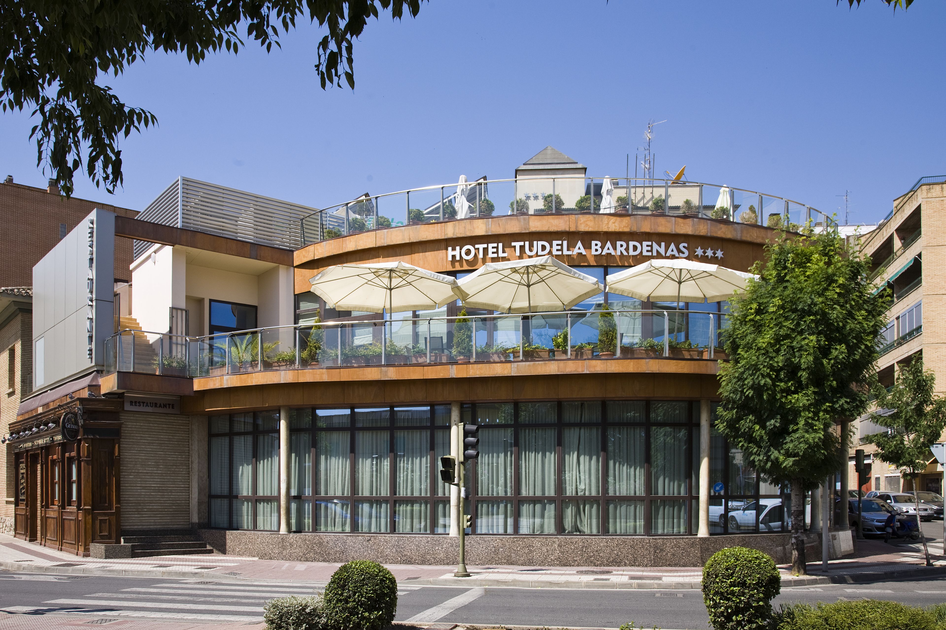 Un hôtel au design moderne, doté d’un balcon avec des parasols et offrant une vue dégagée sur la rue.