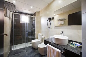 Un baño moderno con ducha de vidrio, inodoro, bidé y lavabo con espejo.