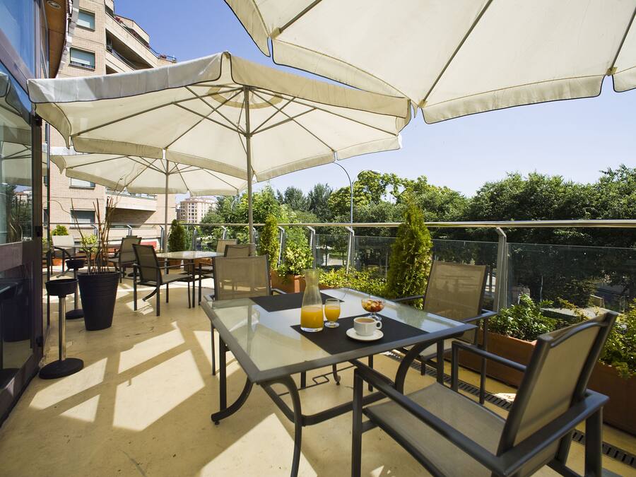 Un patio al aire libre con mesas, sillas, sombrillas y plantas en macetas.