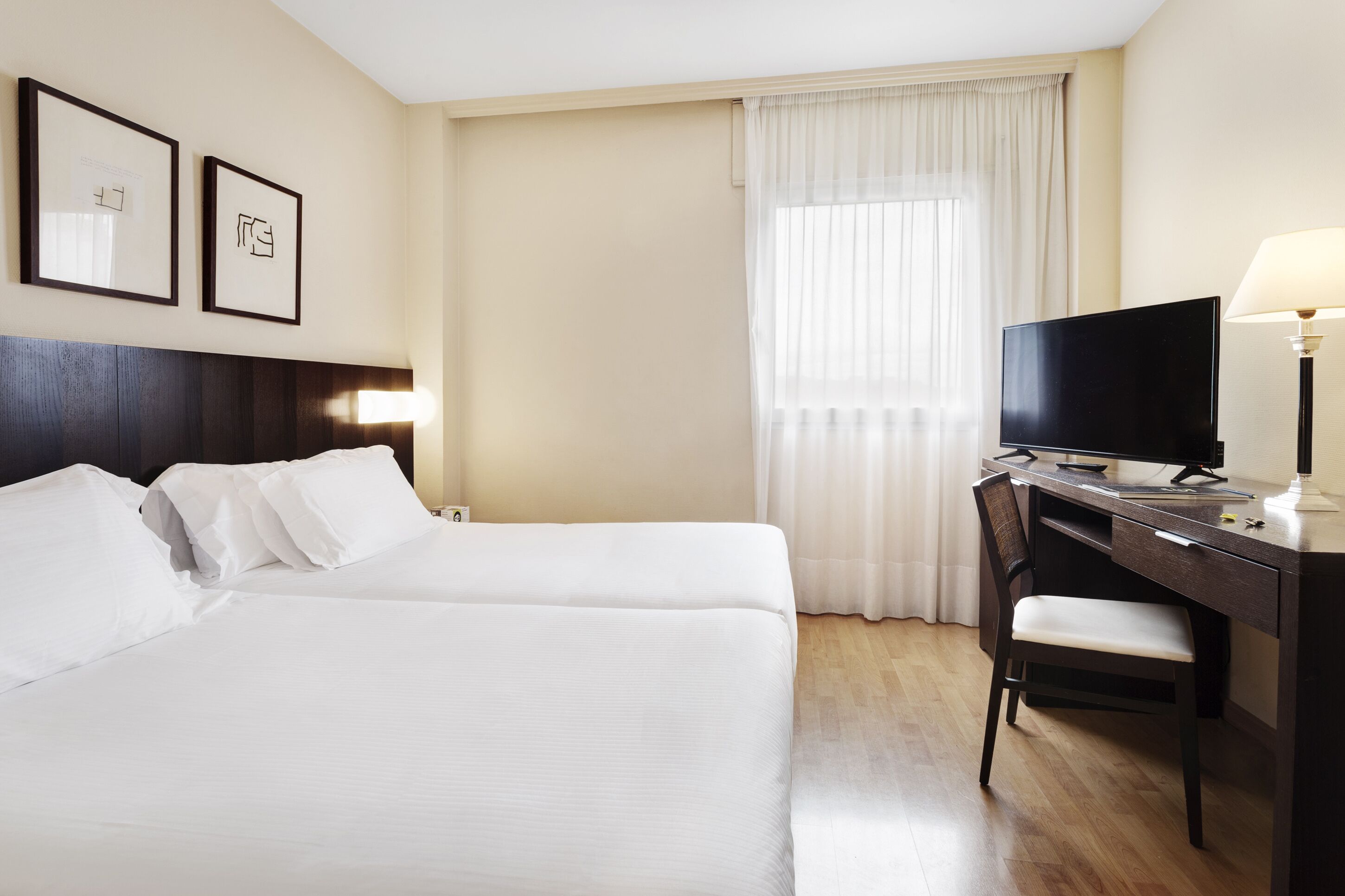 Habitación de hotel con dos camas, un escritorio con silla, televisor y lámpara.