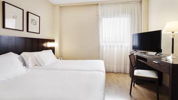 Habitación de hotel con dos camas, un escritorio con silla, televisor y lámpara.
