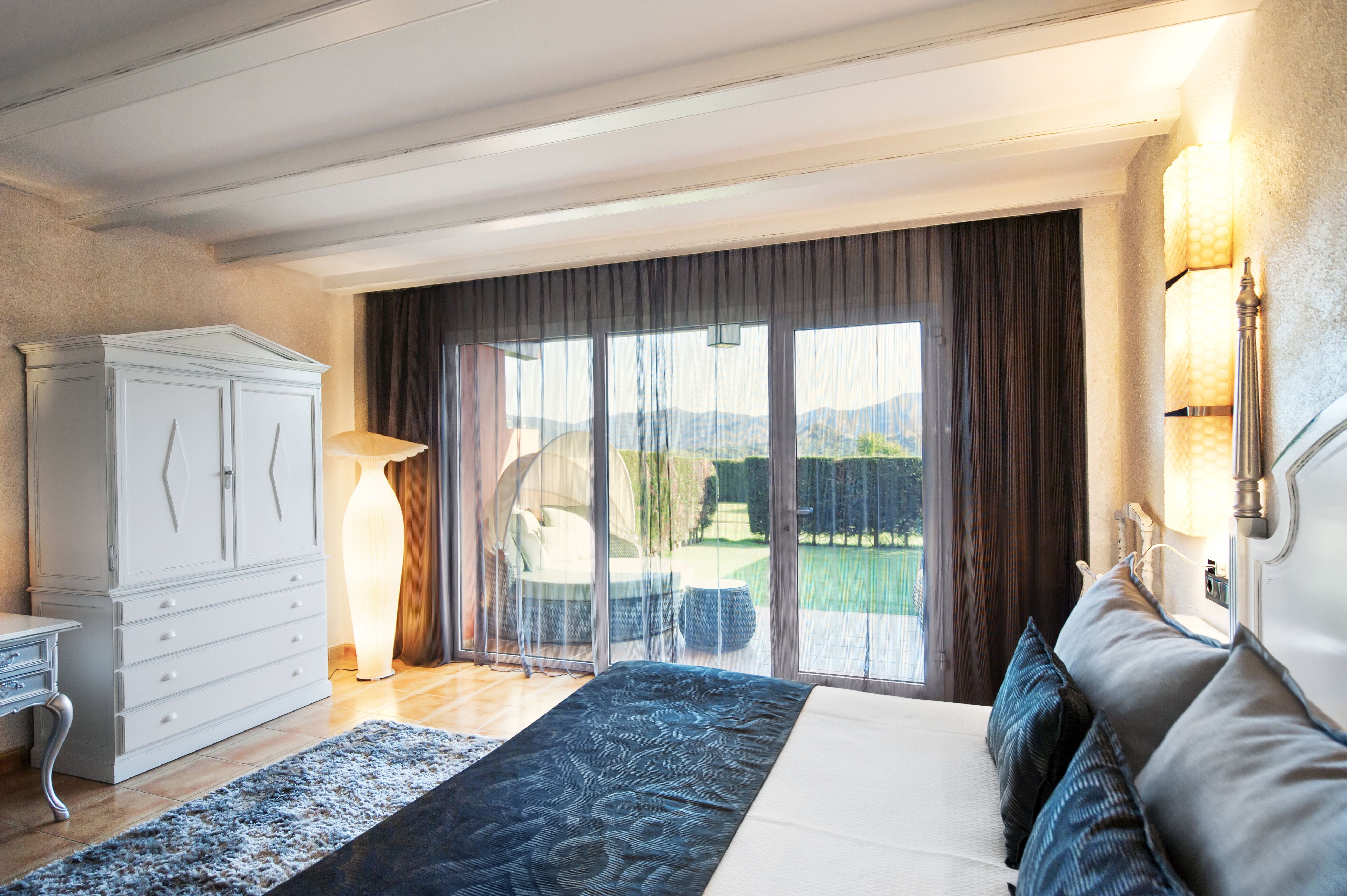 Une chambre avec un lit, une armoire, un bureau et une vue sur une piscine et des montagnes.