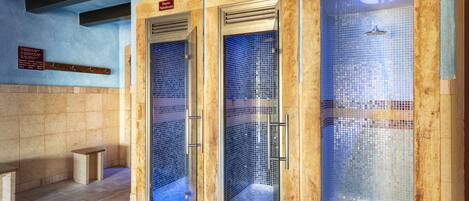 A set of three glass-enclosed shower stalls with tiled walls and a bench to the left.