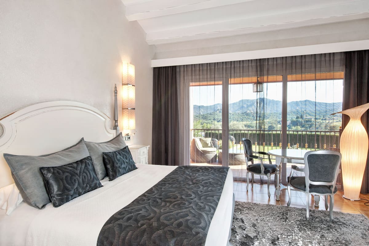 Ein Hotelzimmer mit einem großen Bett, einem Balkon mit Bergblick und einem Essbereich mit Stühlen und einem Tisch.