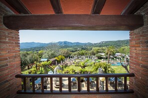Ein Balkon mit Blick auf einen angelegten Garten, ein Schwimmbad und Berge.