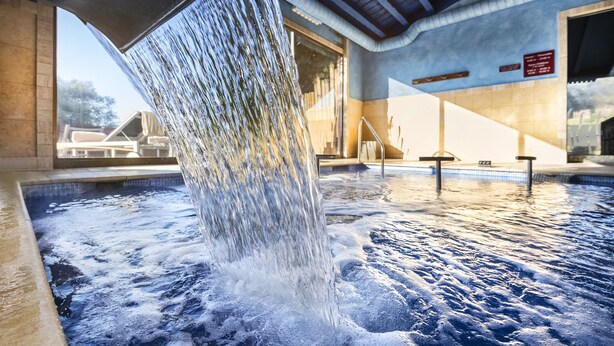 Un bain à remous agrémenté d’une cascade, entouré d’une piscine carrelée et doté d’une entrée couverte.