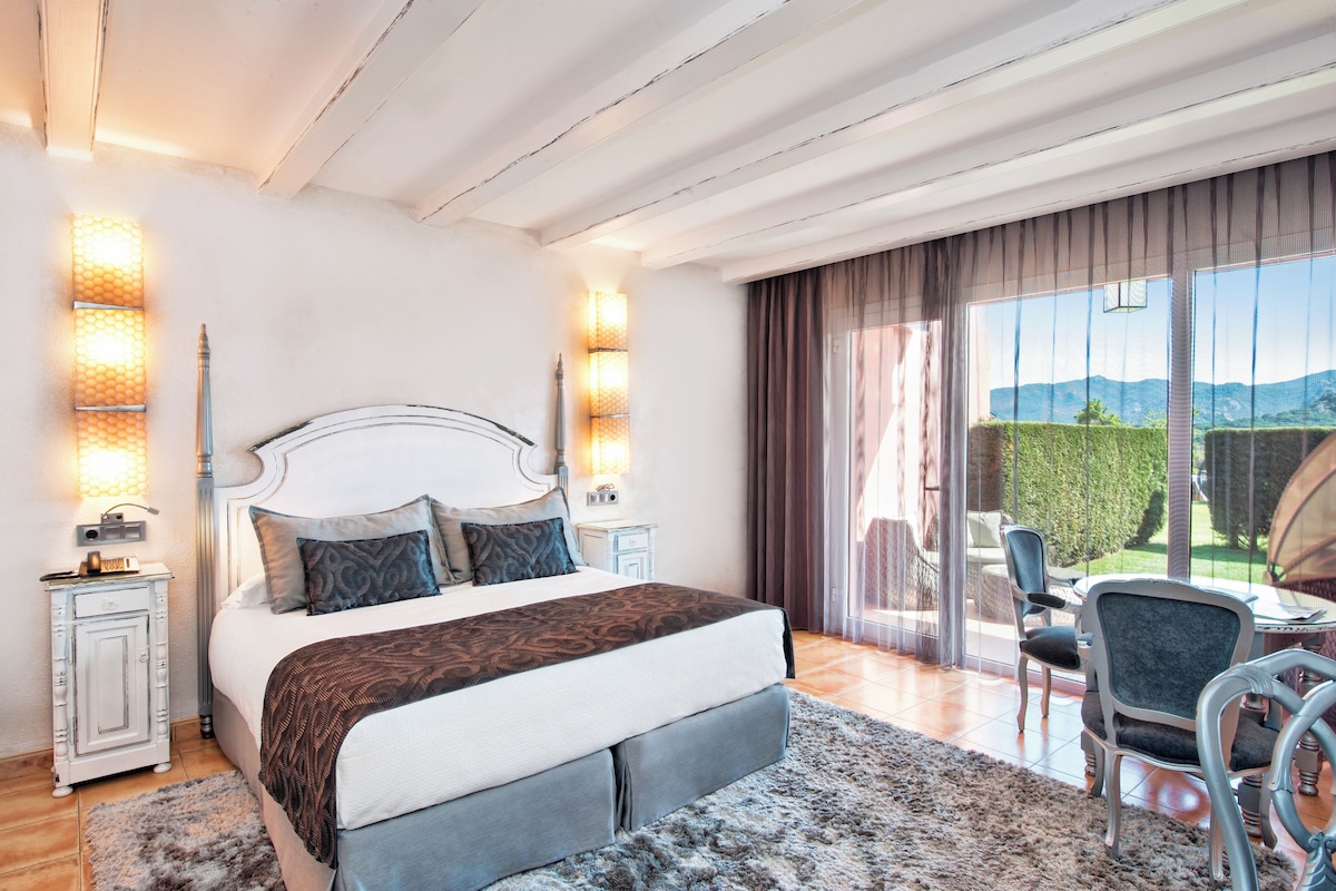 Un dormitorio con una cama grande, lámparas de noche, vistas al exterior y una zona de comedor con sillas.
